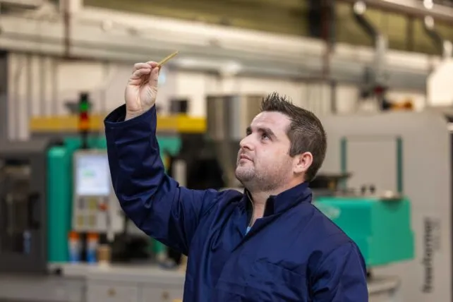 TUS researcher Aarpn Maloney holds up a 3D printed part in the air to examine it.